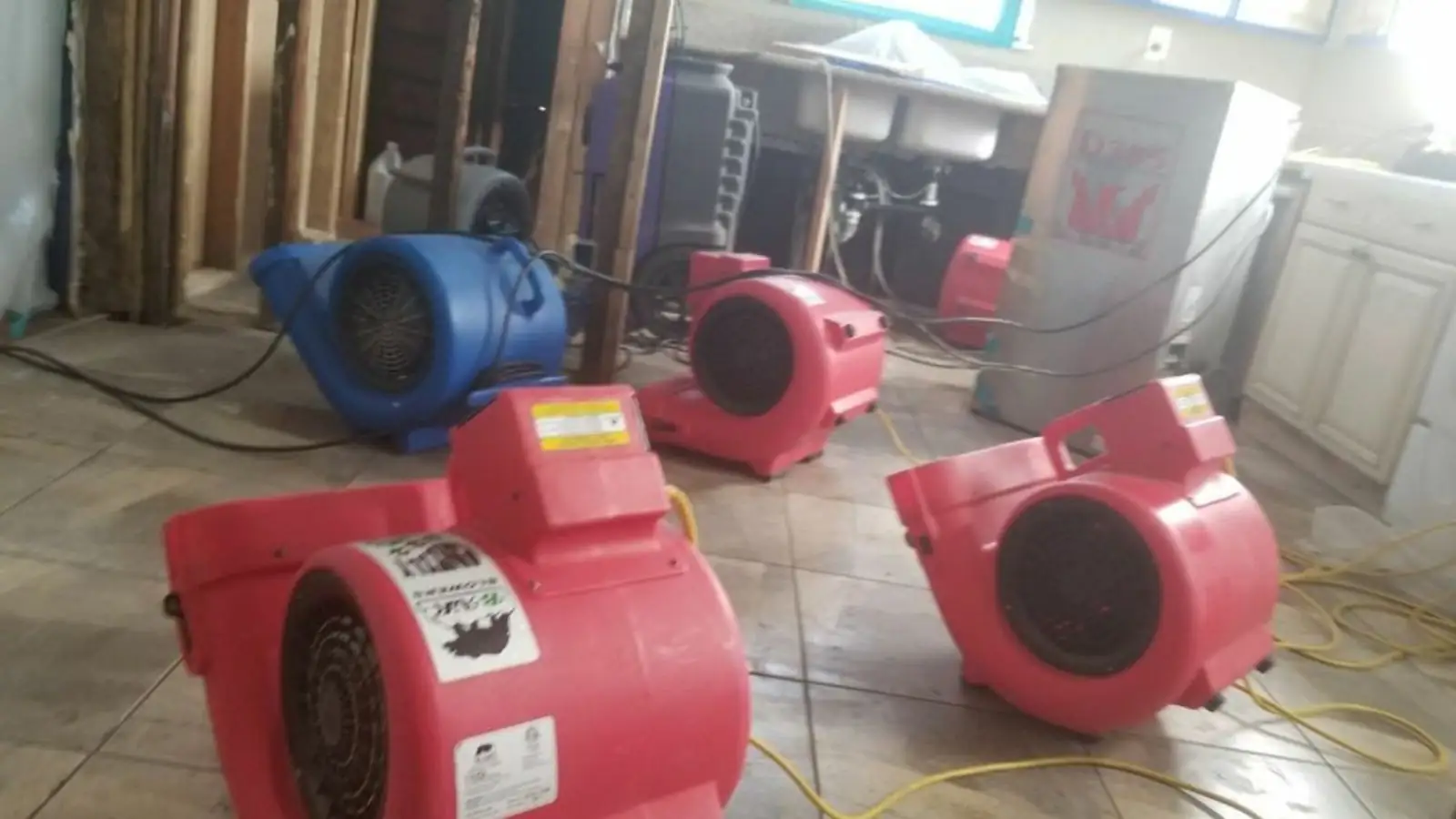 Red air movers running on a tile floor beside opened walls and cabinets