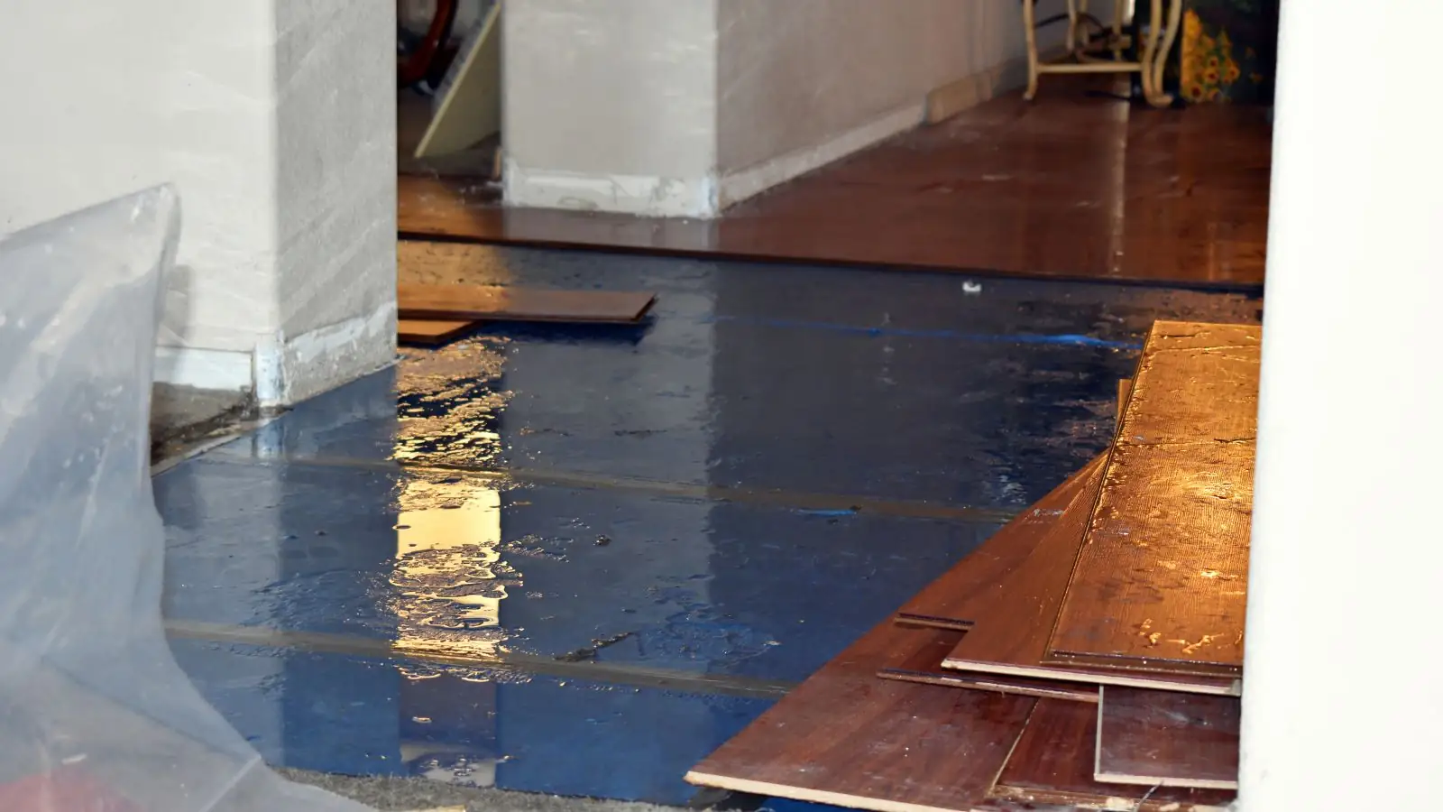 Hardwood boards lifted from a wet subfloor covered with plastic sheeting