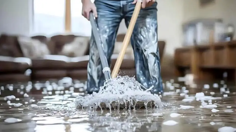 Person mopping a floor with foam and a mop after water damage