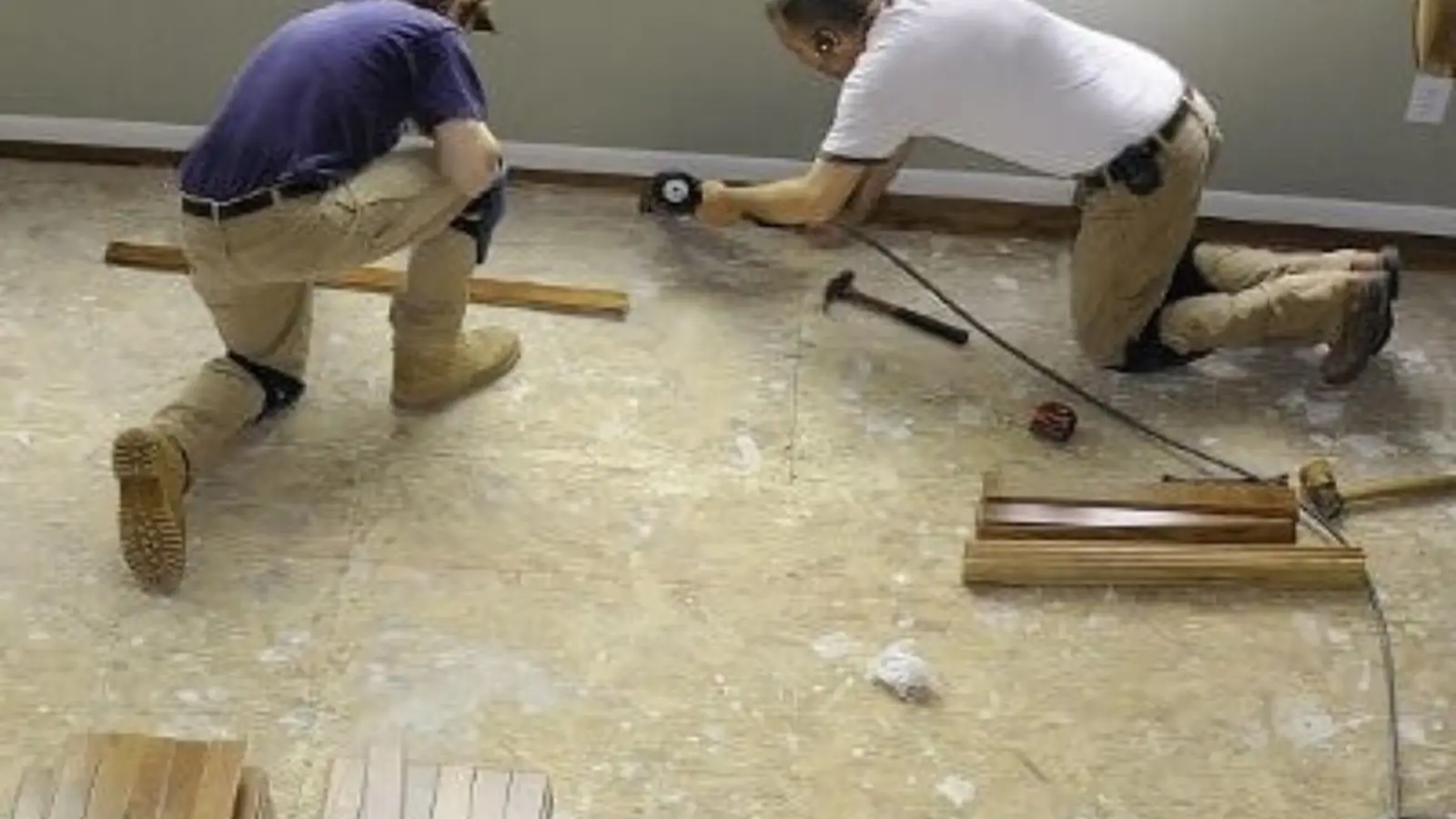 Two contractors kneeling on a damaged floor while removing and repairing flooring